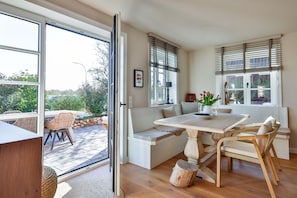 A dining area with a table, chairs, and a bench. There is a view of the outdoors through large windows. - Stylish living with a view of the salt marshes, including a sauna, fireplace, and terrace (Sylt)