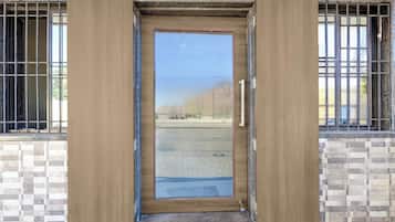 Una puerta de madera con un panel de vidrio, en un edificio con paredes de azulejos y ventanas con barrotes.