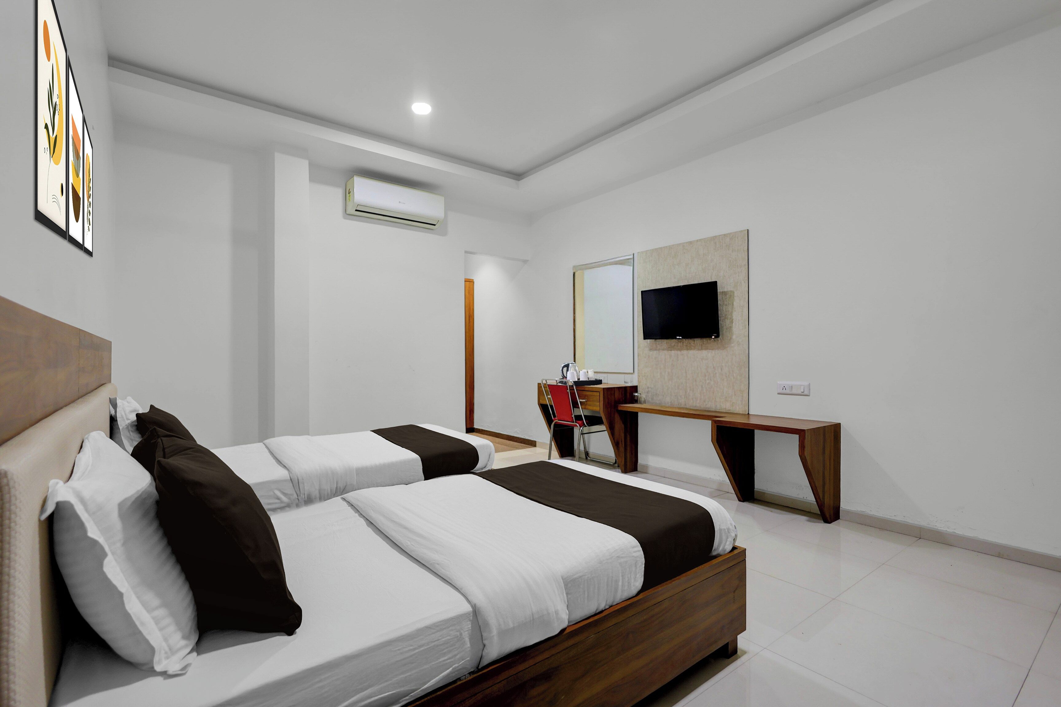 A modern hotel room with two beds, a desk, a chair, a flat-screen TV, and an air conditioning unit.