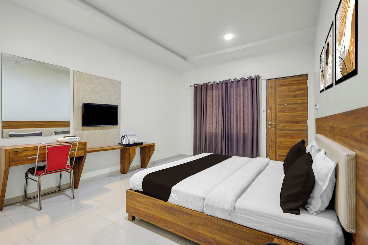 A hotel room with a bed, a desk with a chair, a television, and a window with curtains.
