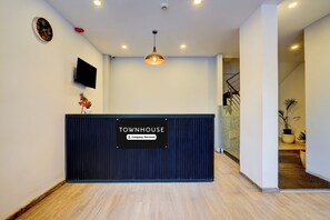 En receptionsdisk med skilt, der angiver virksomhedsservice, et ophængt fjernsyn og en loftlampe.