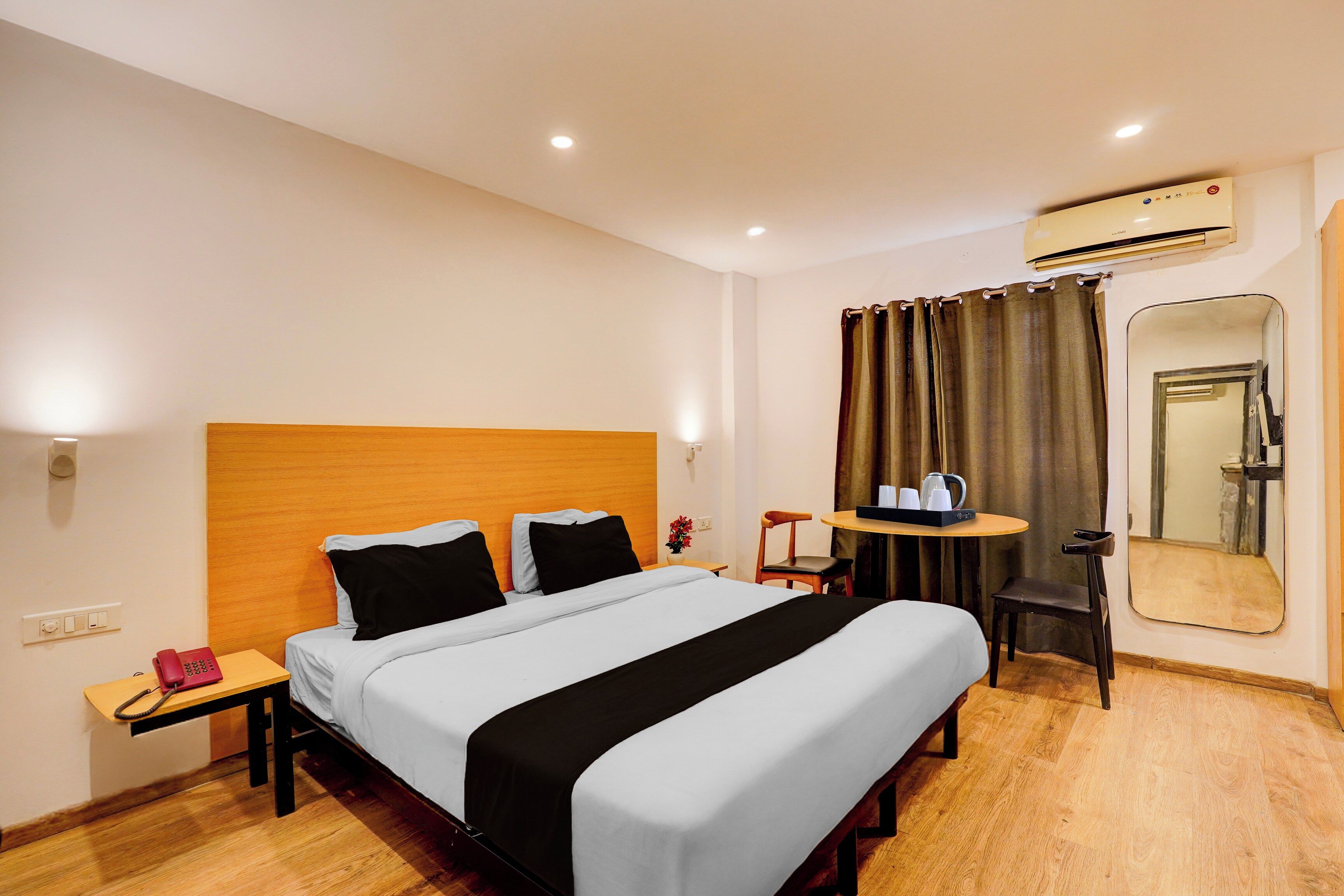 A hotel room with a bed, bedside table, chair, and a small table with a mirror.