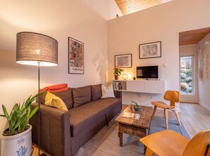 A modern living room with a sofa, a coffee table, a lamp, and a TV. There are framed artworks on the wall and a plant on the floor. - Mt. Tabor Guesthouse | Courtyard & Park Walk (Portland)