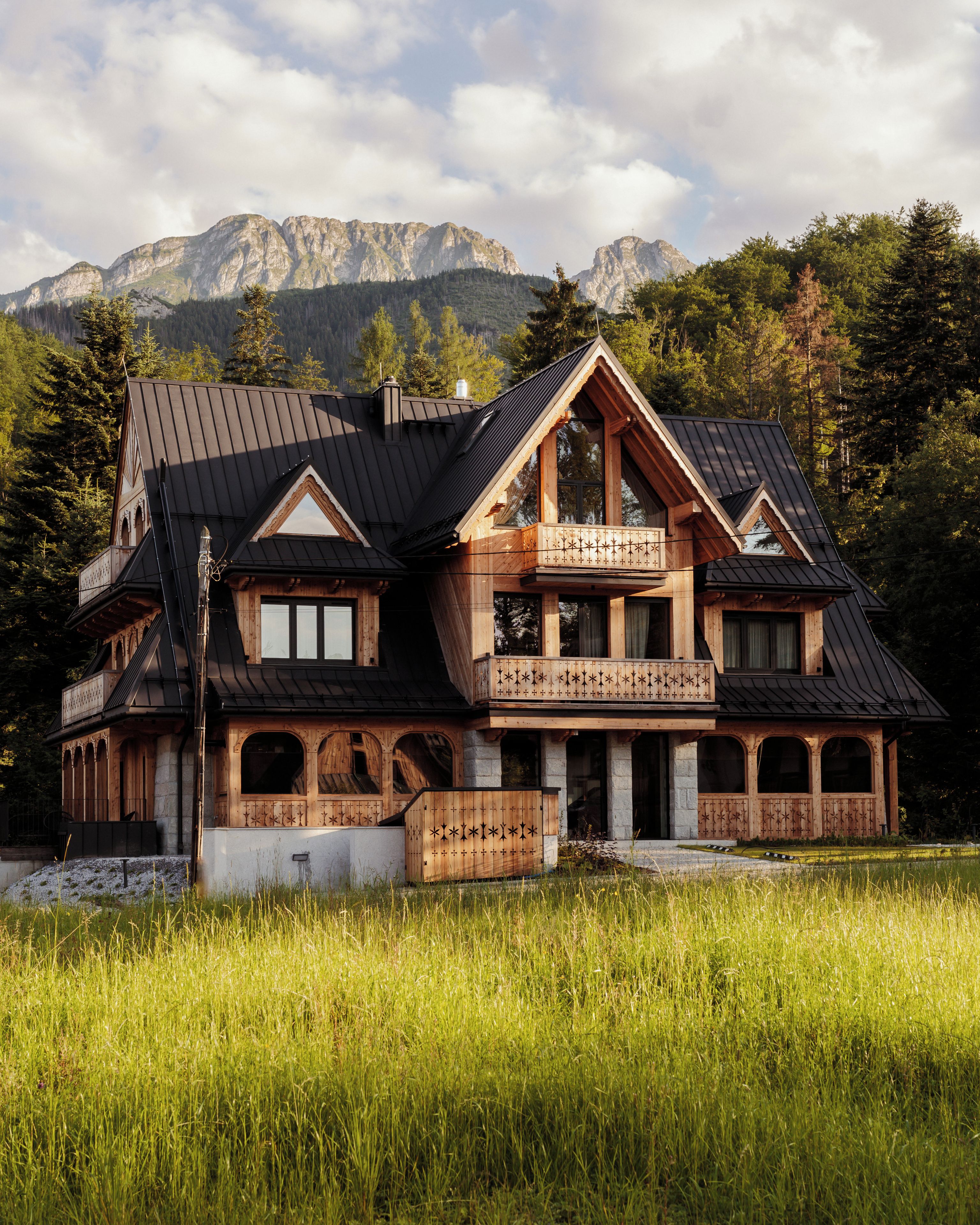 A chalet with a balcony, a stone facade, and a view of mountains.