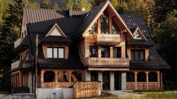 A chalet with a balcony, a stone facade, and a view of mountains.