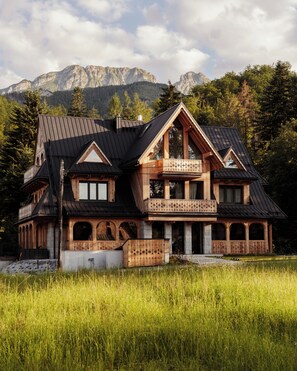 A chalet with a balcony, a stone facade, and a view of mountains.