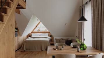 A modern loft bedroom with a sloped ceiling, wooden staircase, and a view of neighboring buildings.