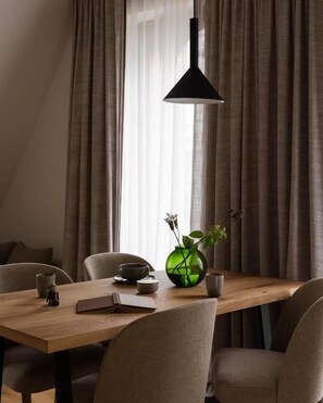 Uma área de refeições com mesa de madeira, cadeiras, um vaso com planta e uma luminária pendente.