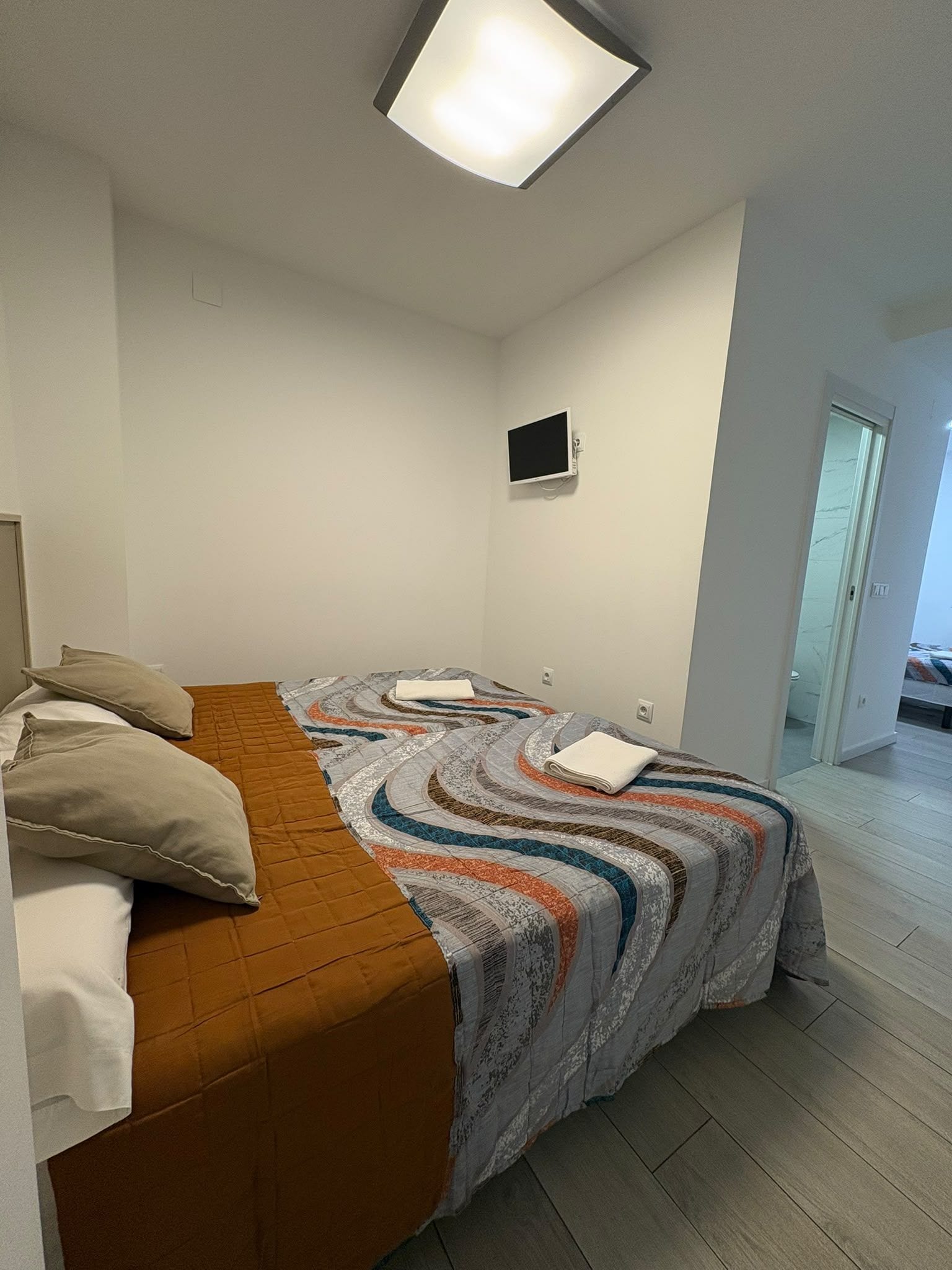 Un dormitorio con cama, almohadas, un televisor de pantalla plana y una puerta que da a otra habitación.