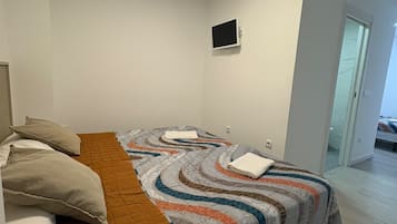 Un dormitorio con cama, almohadas, un televisor de pantalla plana y una puerta que da a otra habitación.