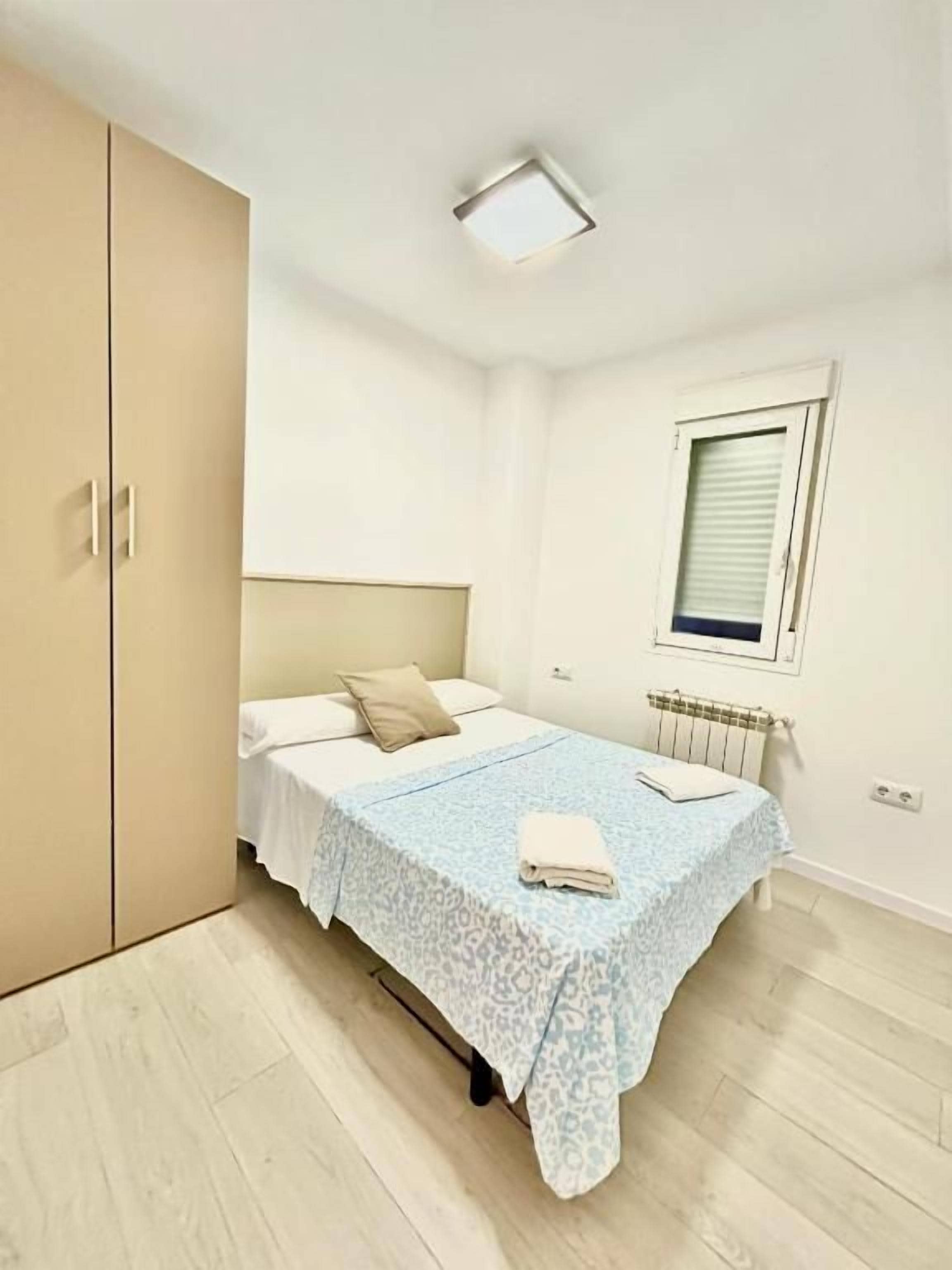 Un dormitorio con cama, armario, radiador y ventana.