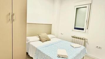 Un dormitorio con cama, armario, radiador y ventana.