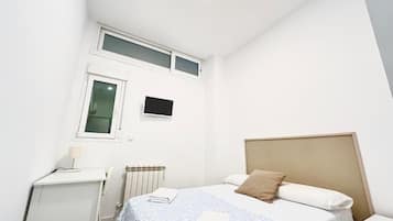 Un dormitorio con cama, escritorio, radiador y ventana.