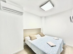 A bedroom with a bed, a bedside table, a nightstand, and a wall-mounted air conditioning unit. - HOSPEDAJE LA PAZ (Madrid)