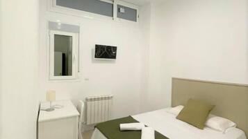 A hotel room with a bed, a desk, a chair, a radiator, and a ceiling light.