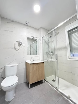 A modern bathroom with a toilet, sink, and glass-enclosed shower. - HOSPEDAJE LA PAZ (Madrid)