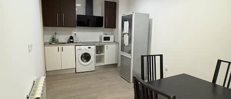 A compact kitchen with a dining table and chairs, a washing machine, and a refrigerator.