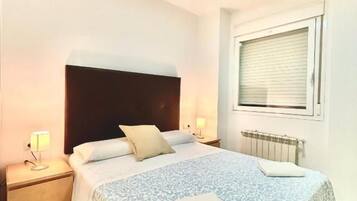 A hotel room with a bed, bedside tables, a window, and a radiator.