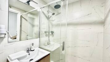 A bathroom with a glass-enclosed shower, a white sink, and a mirror above the sink.