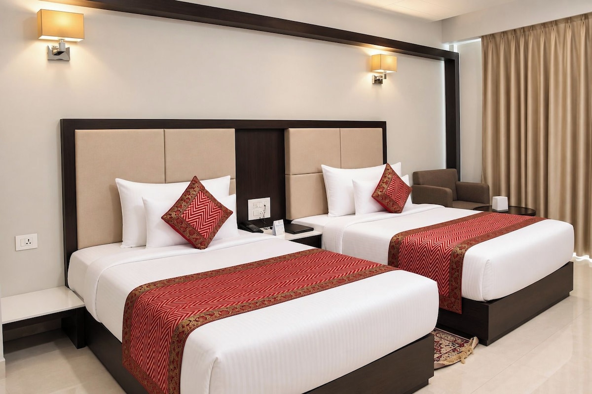 Habitación de hotel con dos camas, un escritorio, una silla y un amplio ventanal con cortinas.