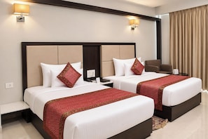 Habitación de hotel con dos camas, un escritorio, una silla y un amplio ventanal con cortinas.