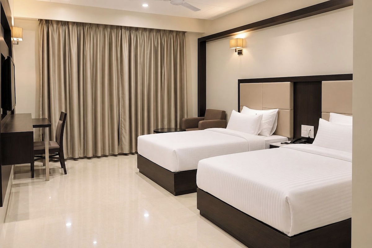 Habitación de hotel con dos camas, un escritorio, una silla y un ventanal con cortinas.