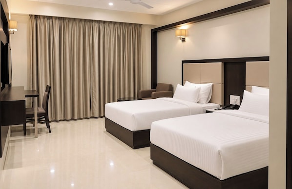 Habitación de hotel con dos camas, un escritorio, una silla y un ventanal con cortinas.