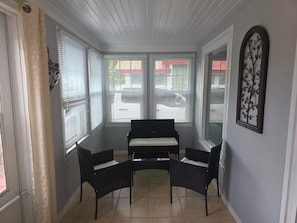 Aurinkoinen olohuone, jossa on musta sohva, kaksi tuolia ja lasinen sohvapöytä.