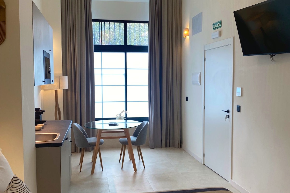 A hotel room with a bed, a desk with a chair, a television, and a window with curtains.