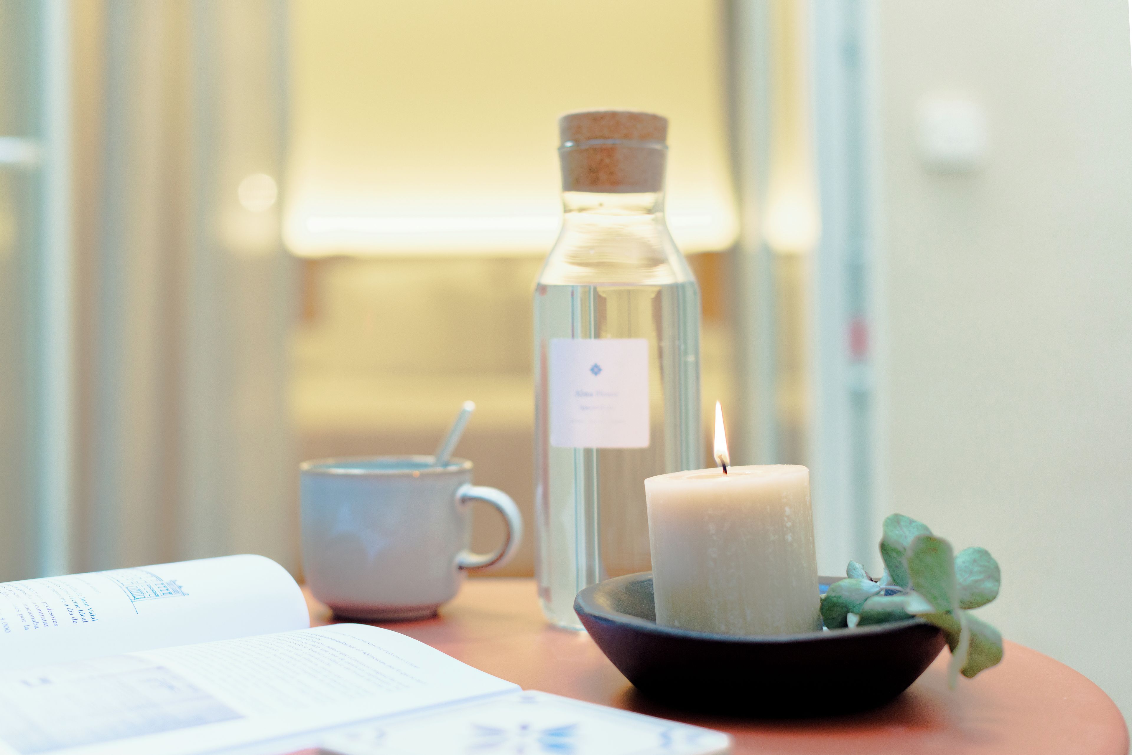 Eine Kerze, eine Glasflasche, eine Tasse und ein Buch auf einem Tisch.