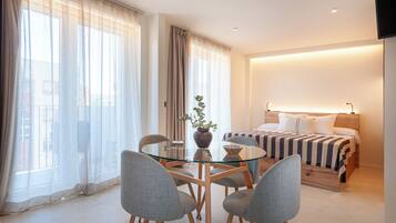 Une chambre d’hôtel comprenant un lit, des tables de chevet, une table en verre avec des chaises et une plante en pot.