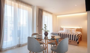 A hotel room with a bed, bedside tables, a glass table with chairs, and a potted plant. - Alma House (Alacant)