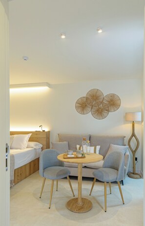 A modern hotel room with a bed, a sofa, two armchairs, a round wooden table, and a decorative wall piece. - Alma House (Alacant)