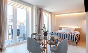 A hotel room with a bed, a glass dining table with chairs, a potted plant, and a view of the outside. - Alma House (Alacant)