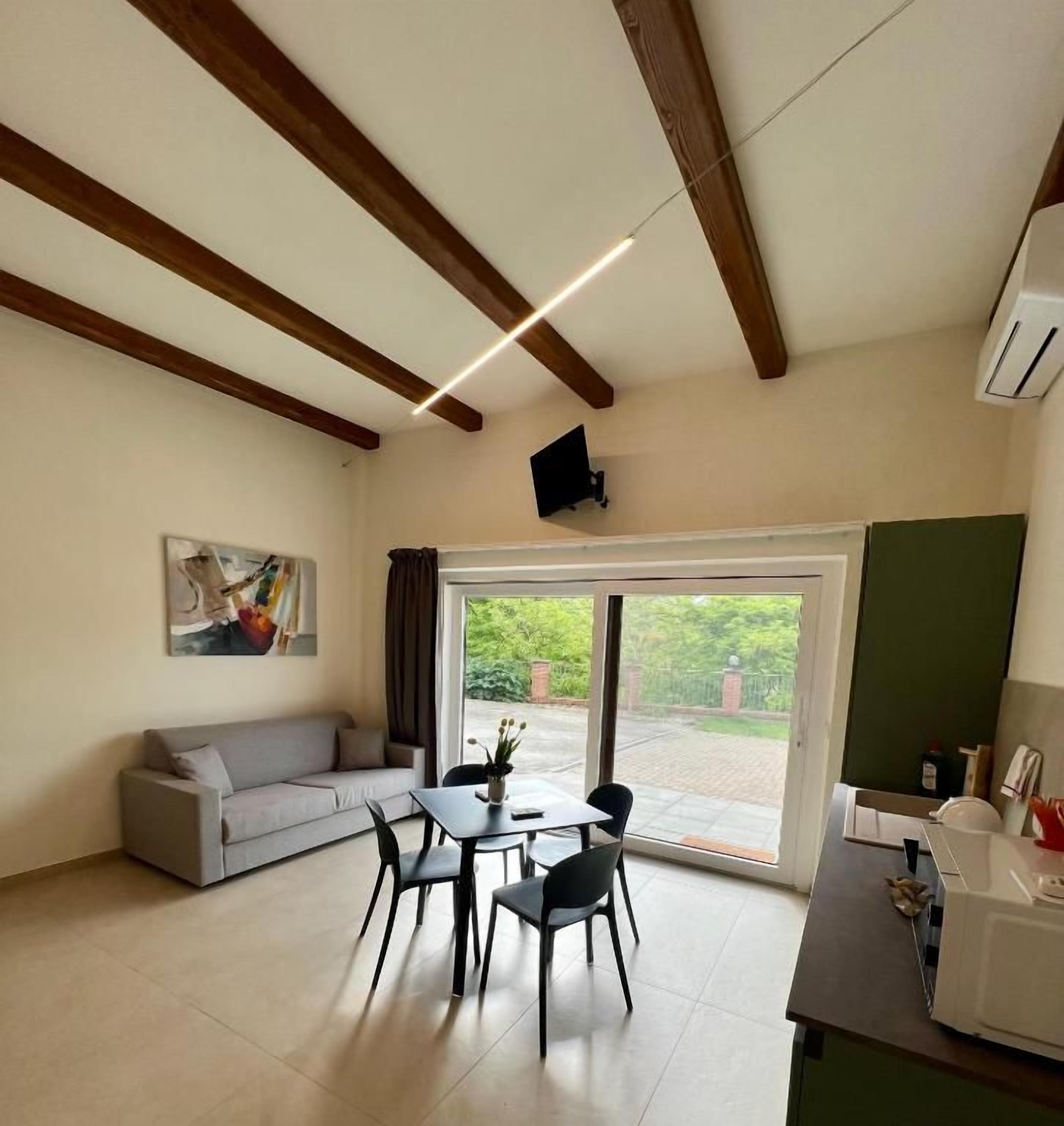 Habitación con sofá, mesa de comedor, sillas, televisor de pantalla plana y un amplio ventanal con vistas a zonas verdes.