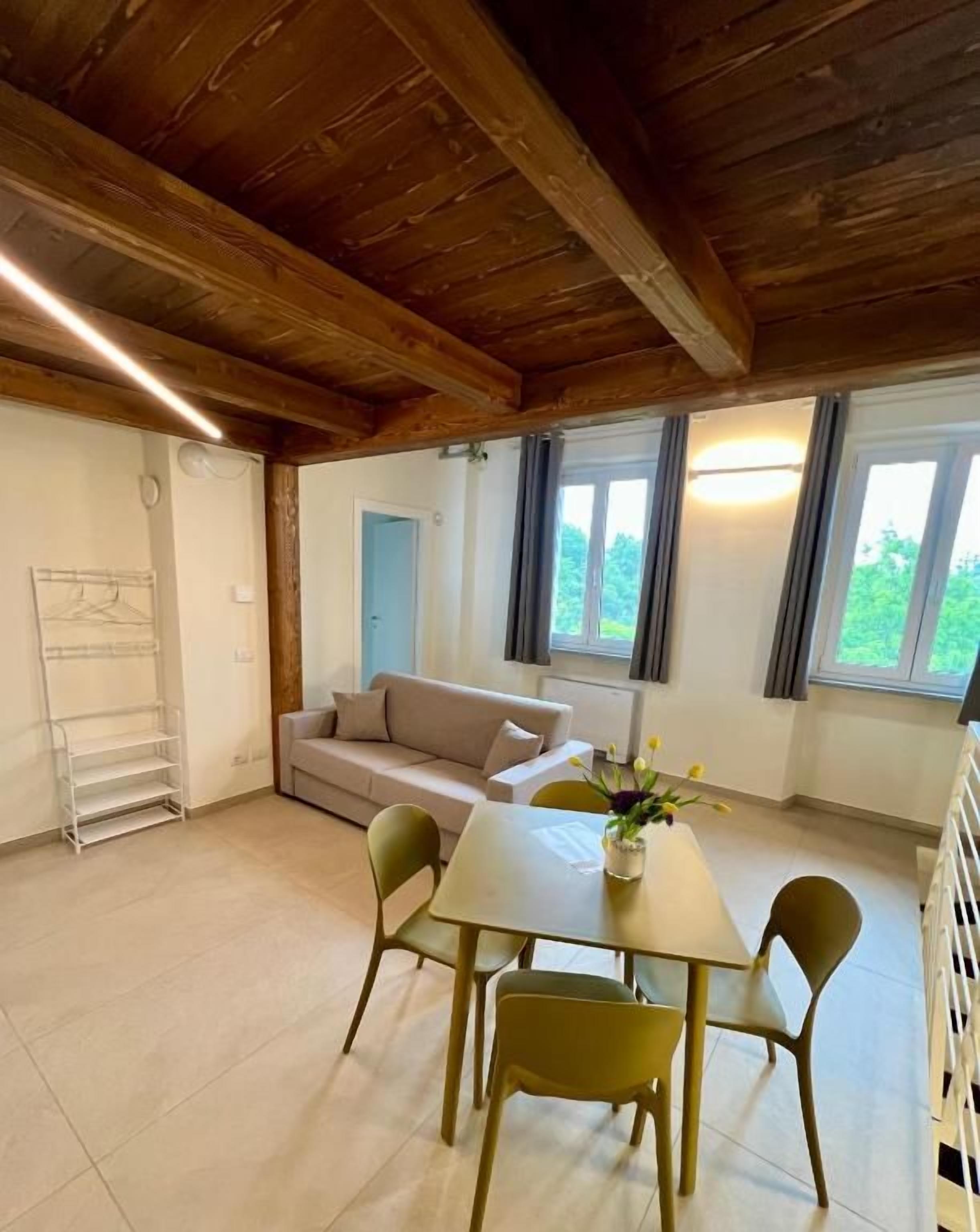 Une pièce avec un plafond en bois, un canapé, une table à manger avec des chaises et une fenêtre avec des rideaux.