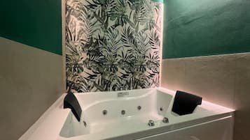 A bathroom with a white bathtub, a green wall, and a leaf-patterned wallpaper.