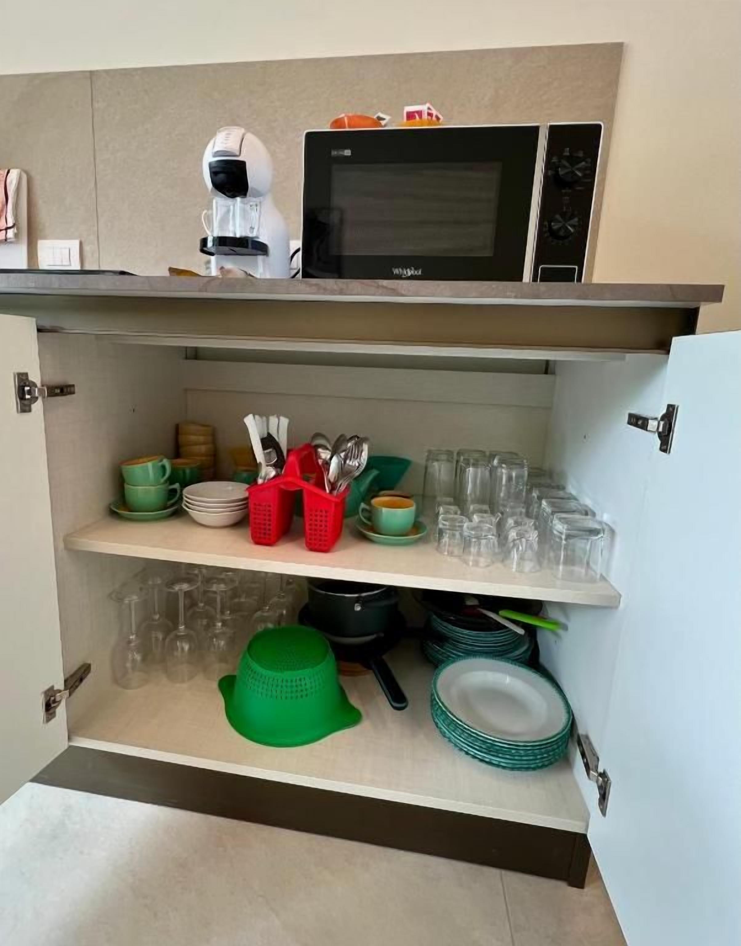 A kitchen with a microwave, a coffee machine, and shelves with dishes and glasses.