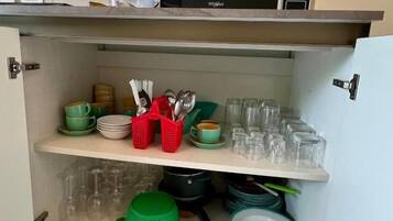 A kitchen with a microwave, a coffee machine, and shelves with dishes and glasses.