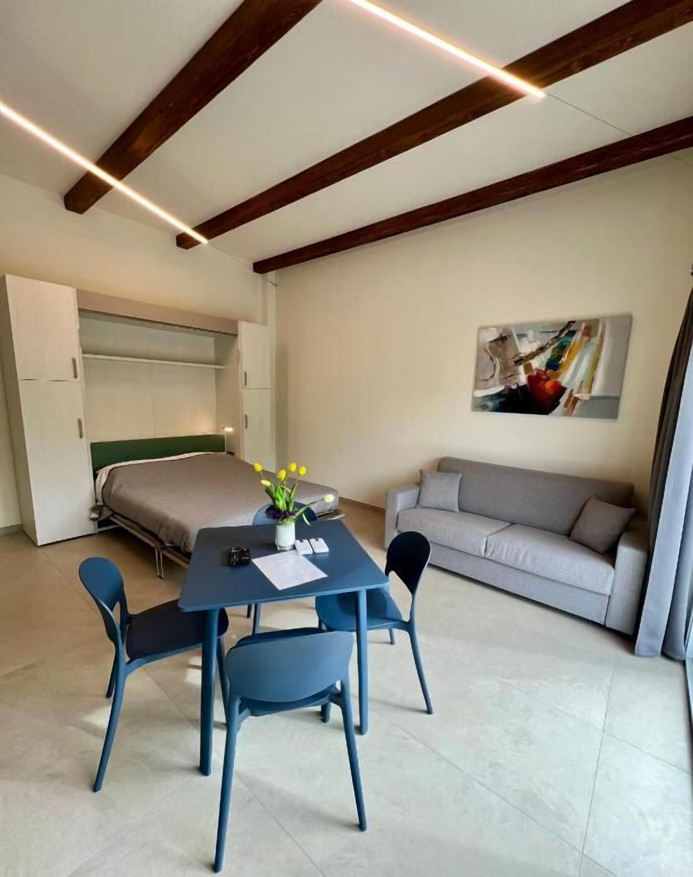 Una habitación compacta con cama, sofá, mesa de comedor con sillas y un cuadro en la pared.