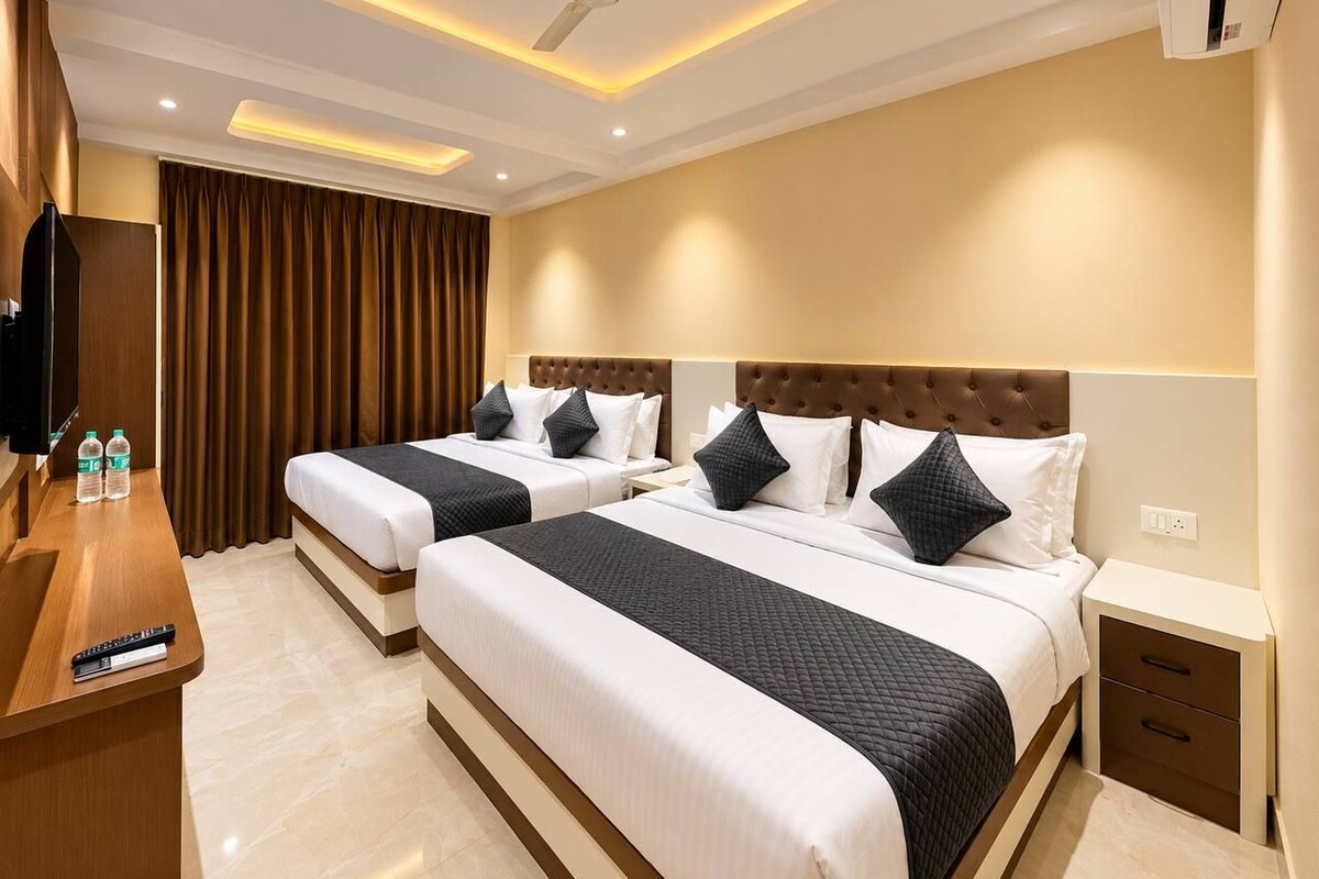A hotel room with two beds, a desk with a TV, and a ceiling fan.