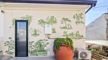 Fachada de un edificio con una puerta, unidad de aire acondicionado instalada en la pared y una planta grande en maceta.