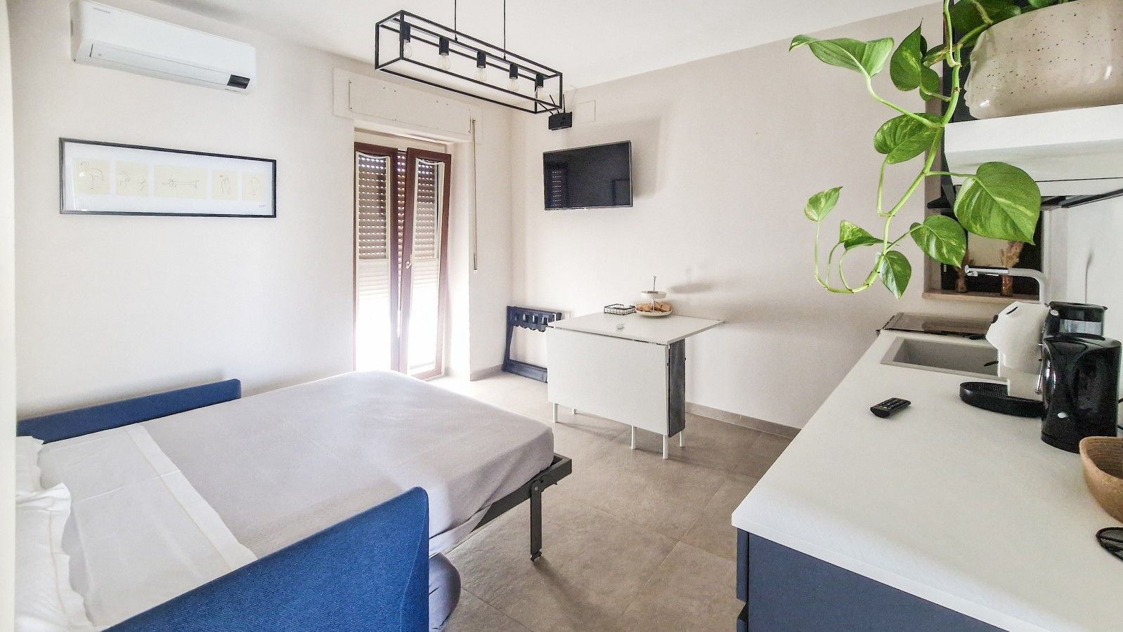 Una camera d'albergo con un letto, una scrivania, una macchina del caffè e una pianta.