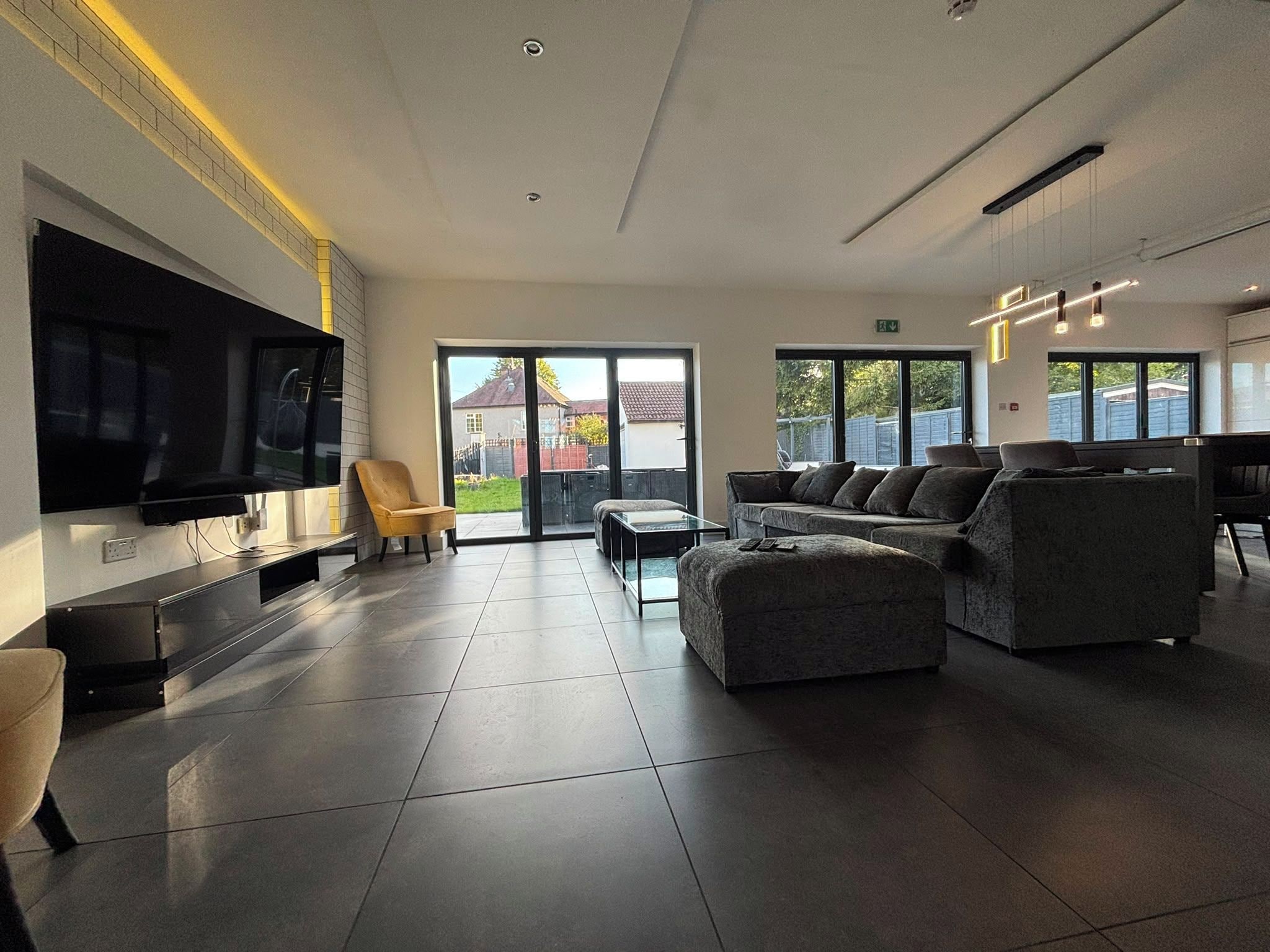 A modern living room with a flat-screen TV, a sofa, a chair, and a dining area with a table.