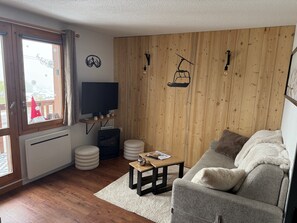 A cozy living room with a wooden wall, a television, a sofa, and a small table. - New Listing (Les Avanchers-Valmorel)