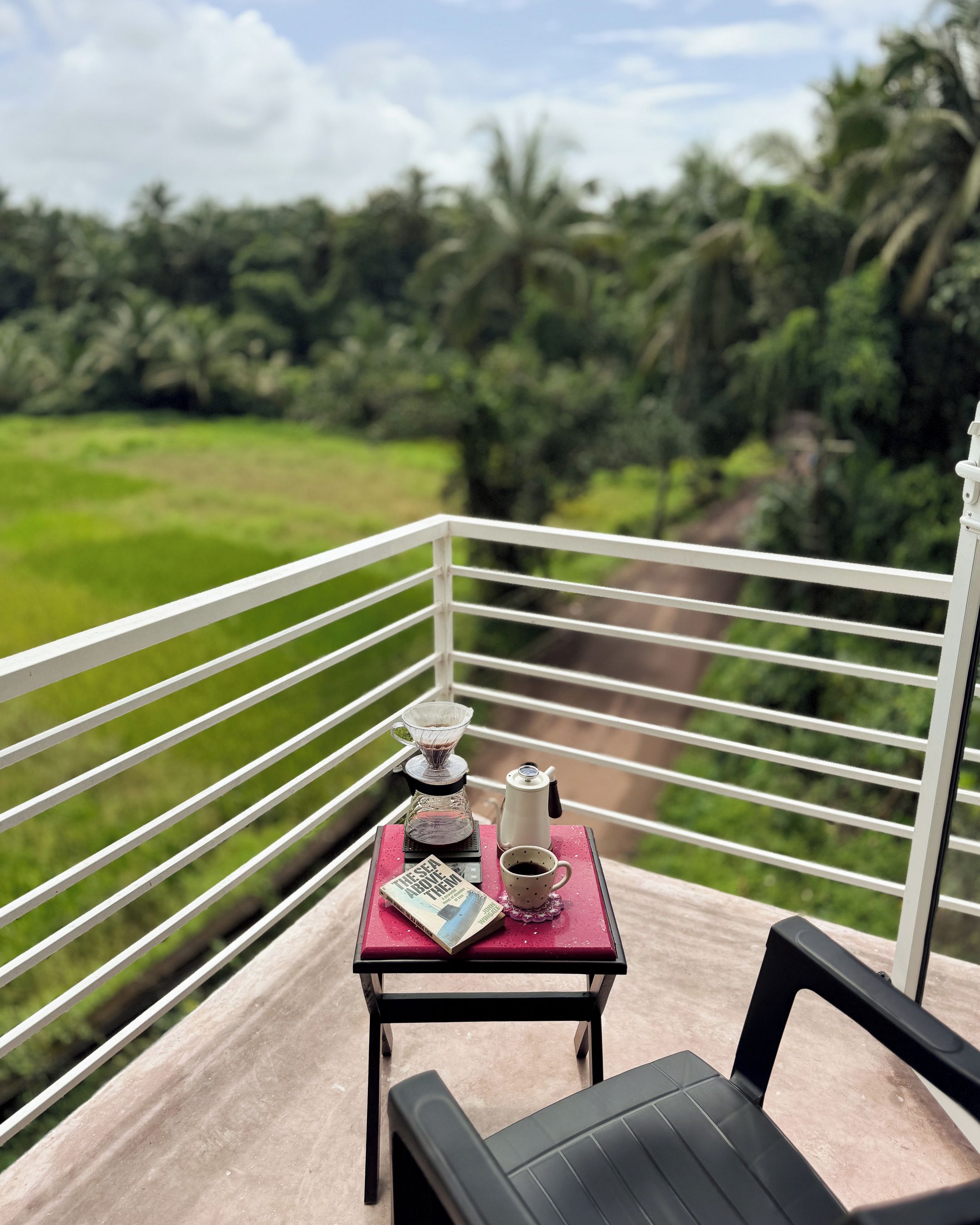 A balcony with a table set for two, a book, a coffee pot, and a cup.
