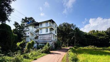A multi-story building with a staircase on the left, surrounded by greenery and a clear sky.