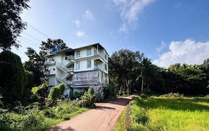A multi-story building with a staircase on the left, surrounded by greenery and a clear sky.