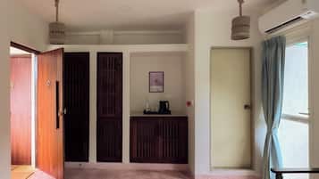 A room with a pink carpet, wooden doors, a small kitchenette, and a window with curtains.