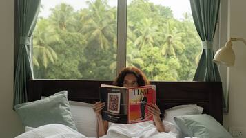 A person lying in bed reading a TIME magazine, with a view of palm trees through a window.